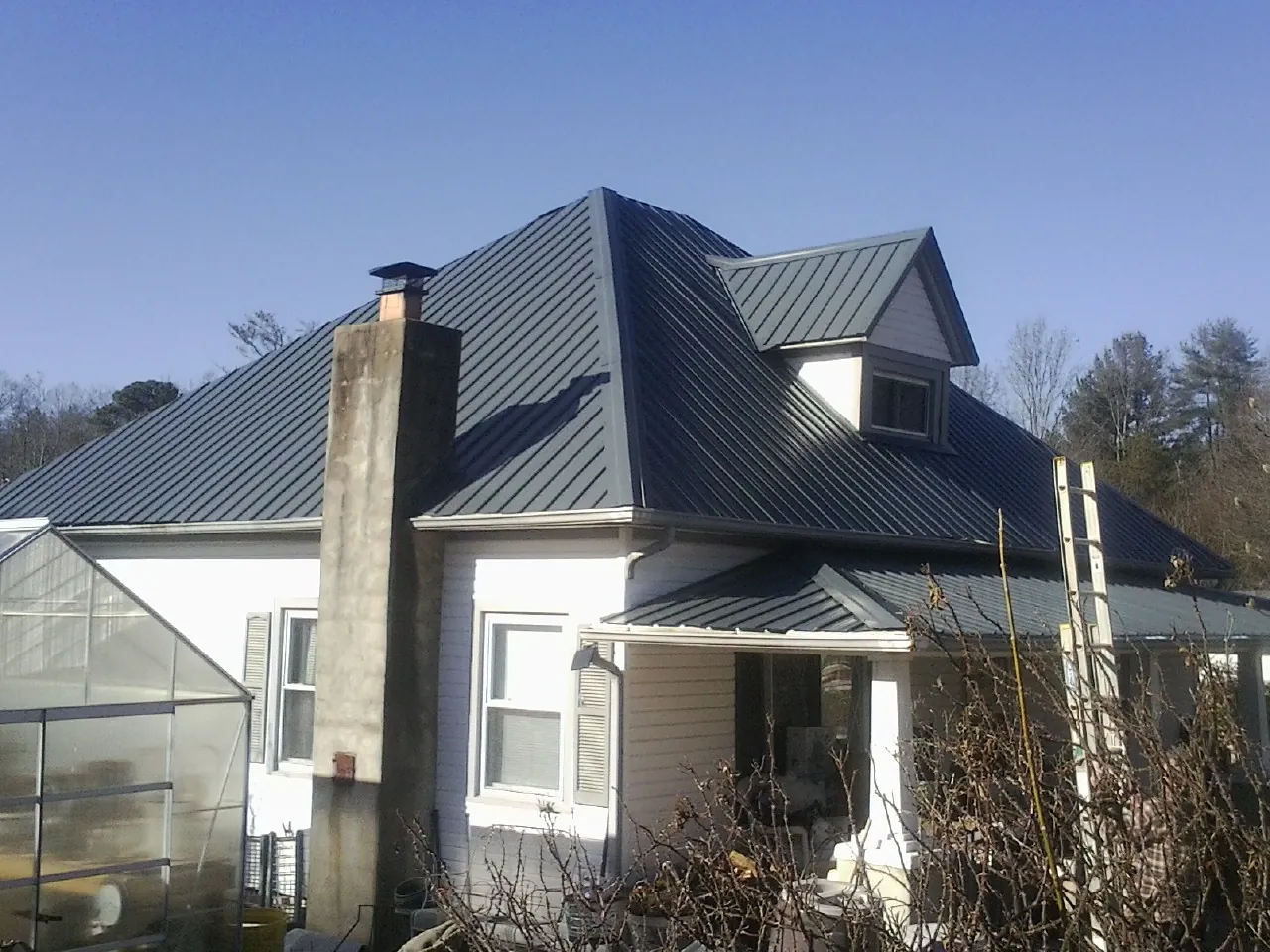 Dark blue standing seam metal roof on a white farmhouse with dormer — Slate & Tile Roof Repair by Roofing Brothers in Kelly