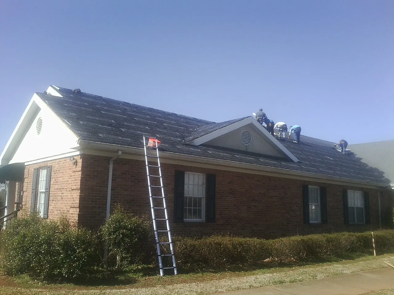 Crew tearing shingles off a brick ranch roof with a ladder set — Emergency Roof Repair work by our crew in Kelly