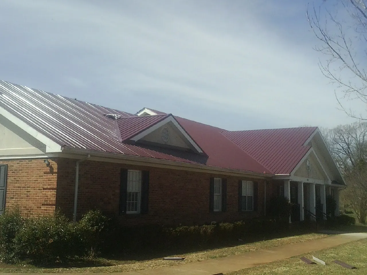 Red metal roof with gabled entries on a long brick building, from a Hail Damage Roof Repair job in Kelly