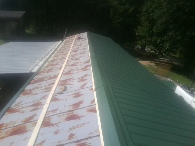 Old rusted panels beside newly installed green metal roofing — Wind Damage Roof Repair by Roofing Brothers in Kelly