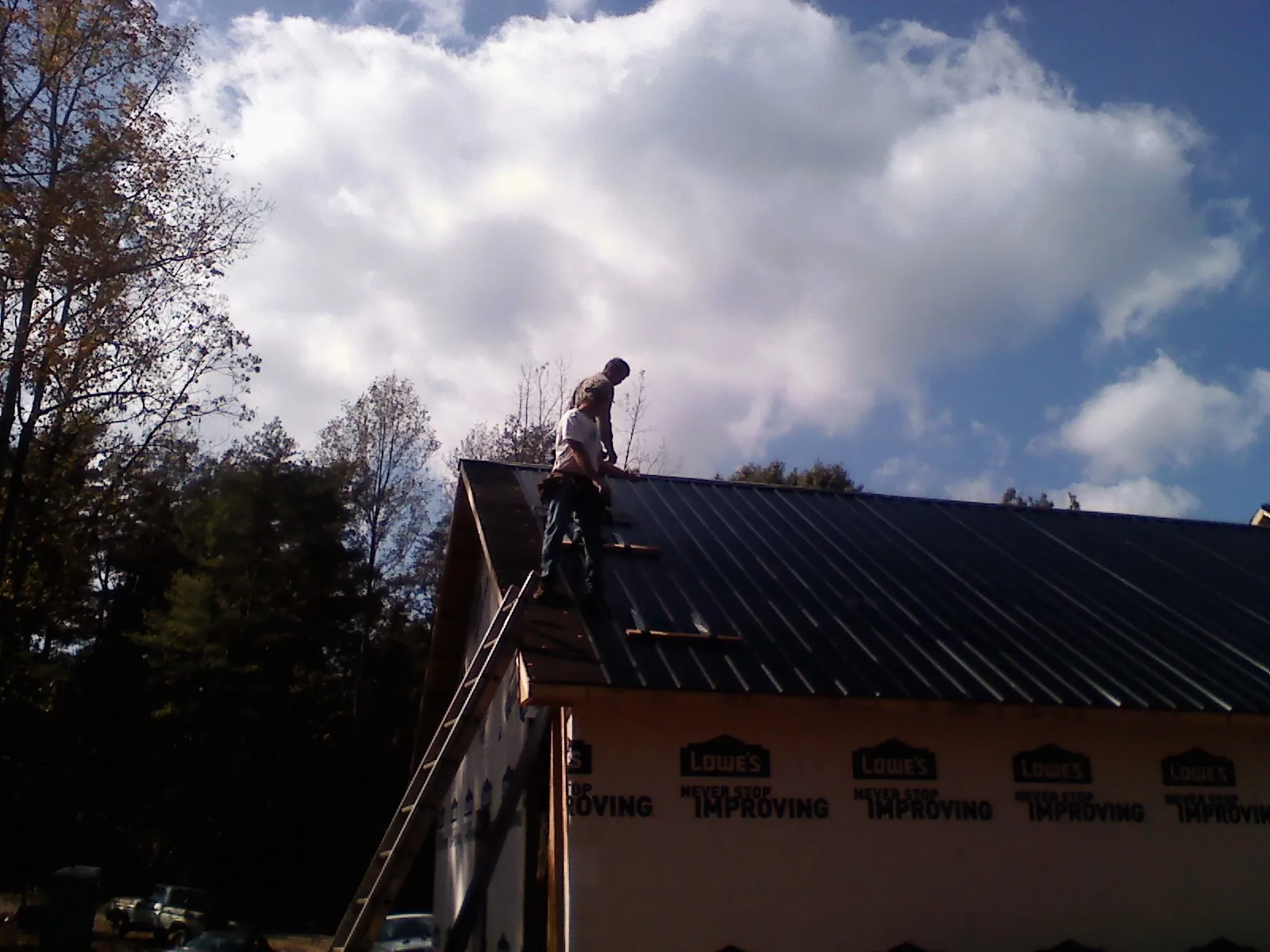 Roofer fastening dark metal panels high against a cloudy sky, from a Roof Inspection job in Kelly
