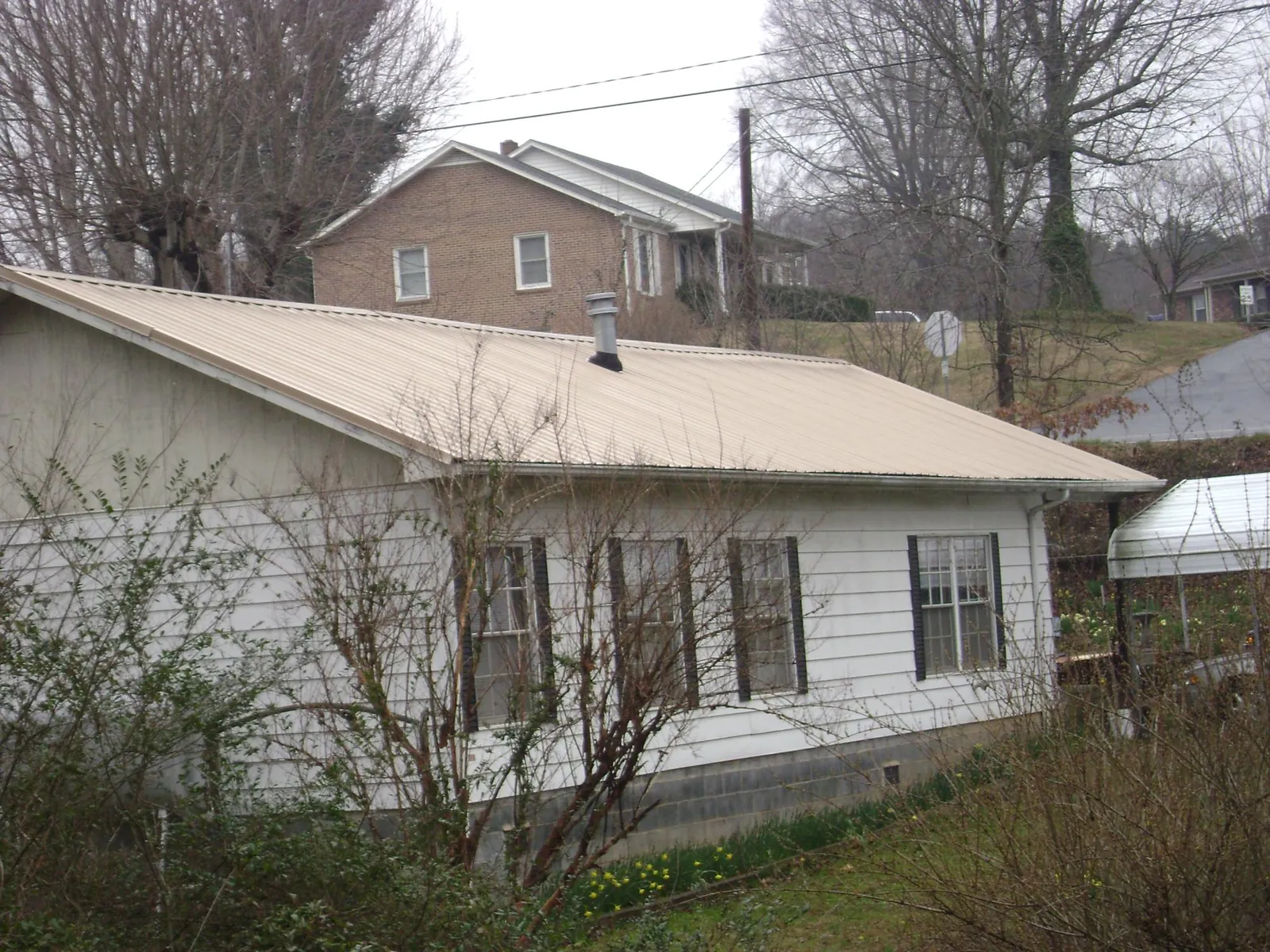 Tan metal roof on a white sided house set into a hillside — Commercial Roofing by Roofing Brothers in Kelly