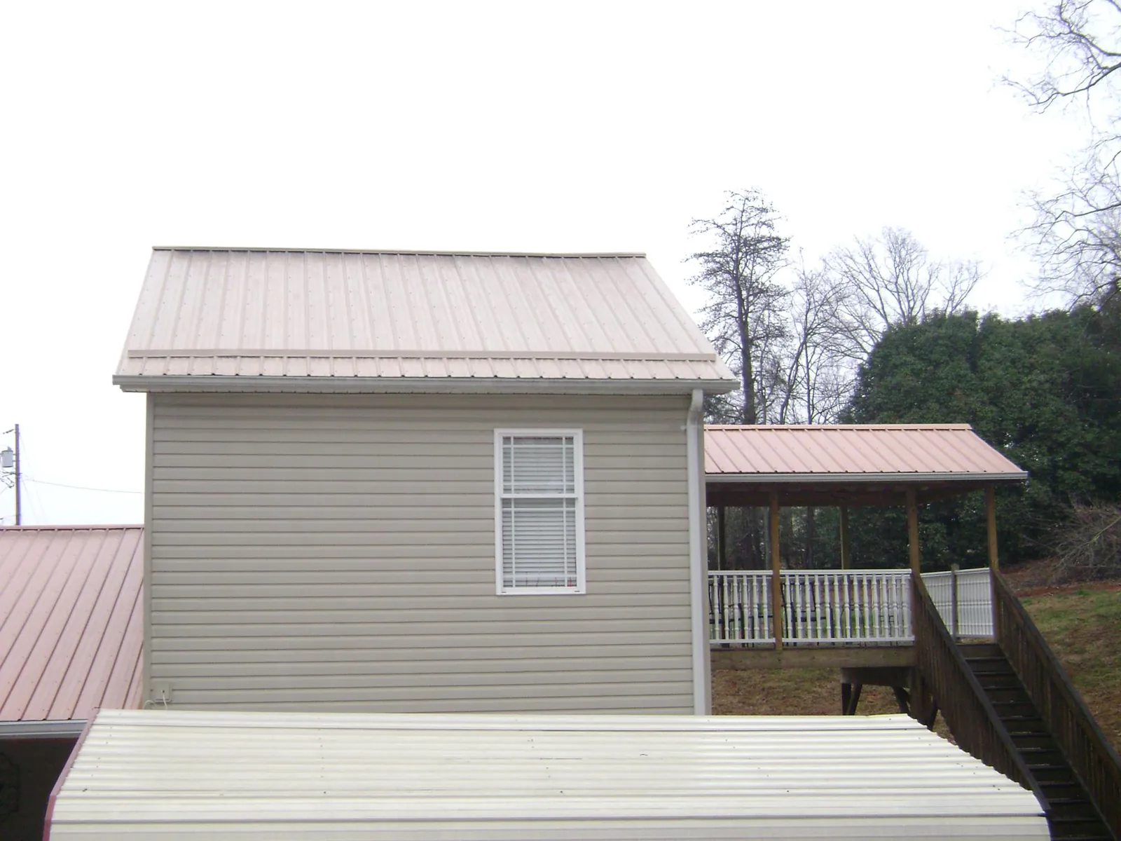 Tan metal roofs on a two story addition and attached porch, from a Roof Replacement job in Kelly